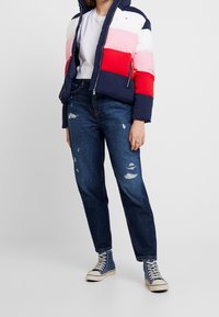 Colorful puffer jacket with navy, pink, red, and white panels, paired with distressed dark blue jeans and blue high-top sneakers.
