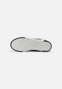 Sneaker sole in black and white rubber. Features a textured surface with horizontal and vertical grooves for traction.