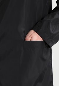 Sort vandtæt frakke med en glat overflade, der har en lomme på venstre side og et enkelt, funktionelt design.