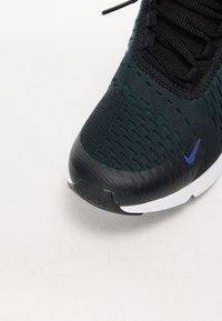 Czarny i zielony but sportowy z teksturowaną siateczkową cholewką, sznurowanym wzorem i białą podeszwą z czarnym gumowym akcentem.