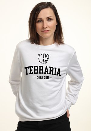 Hvid langærmet sweatshirt med et sort "TERRARIA" logo og teksten "Siden 2011," lavet af et blødt og glat stof.