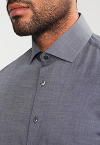 Grå skjorta med knäppning i strukturerad tyg, med klassisk krage och två knappar på frampartiet.