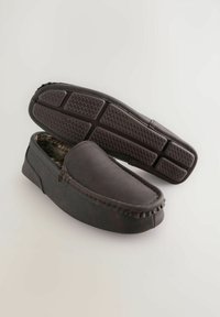Bruine leren moccasin-slippers met een zachte bontvoering, rubberen buitenzool met een gestructureerd grippatroon en een gestikte afwerkingsdetail.