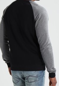 Svart och grå sweatshirt med långa ärmar och ribbade manschetter; har en tvåfärgad design och en rund halsringning. Bärs över denimjeans.