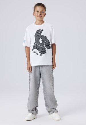 Weißes T-Shirt mit einem schwarzen Grafiken eines Hasenkopfes und Blitzen. Kombiniert mit hellgrauen, lockeren Jeans und weißen Sneakers.