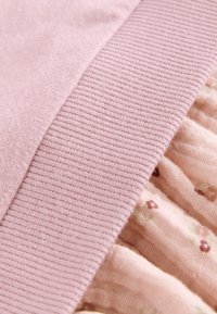 Nahaufnahme eines weichen, rosa Strickstoffs mit Rippenstruktur neben einem gerafften, leichten rosa Stoff mit kleinem Blumenmuster.