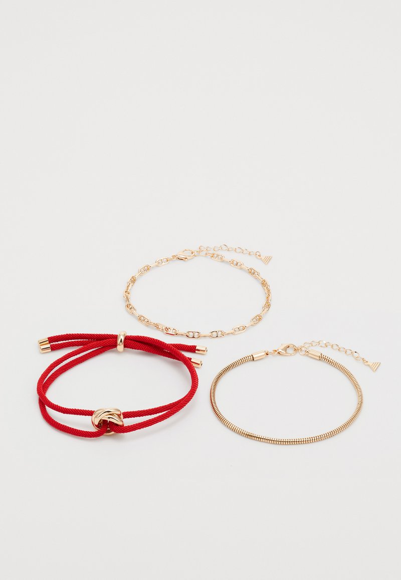 Trois bracelets : un bracelet en corde rouge avec un accent doré, un bracelet en chaîne dorée et un bracelet en fil doré flexible avec un fermoir.