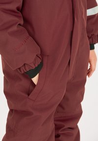 Bordeaux kleurig geïsoleerd overall met elastische manchetten, zijzakken en reflecterende accenten, gemaakt van weerbestendig materiaal.