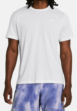 Man draagt een eenvoudig wit T-shirt met korte mouwen en blauw-paarse tie-dye shorts, staand tegen een witte achtergrond.