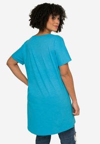 Camiseta turquesa de manga corta, de corte relajado, con escote redondeado y textura suave, combinada con vaqueros de mezclilla.