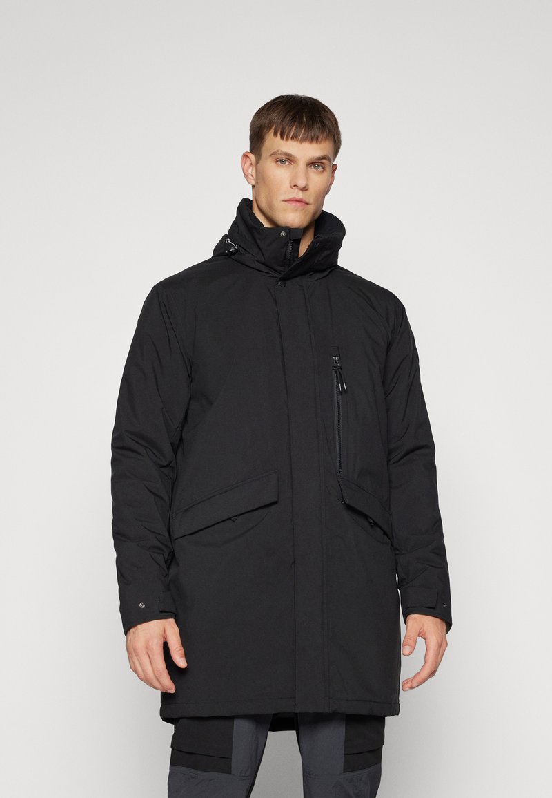 Geacă parka izolată, de culoare neagră, cu guler înalt, fermoar frontal, buzunare laterale și un buzunar pe piept cu fermoar. Textură netedă, design până la genunchi.