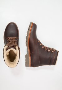 Botas de tornozelo em pele castanha com atacadores à frente, forro de lã creme e sola de borracha cinza robusta com um pequeno salto.
