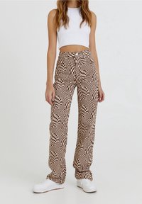 Bruine en crèmekleurige broek met een geruit patroon, hoge taille en rechte pijpen, gecombineerd met een witte crop top en witte sneakers.