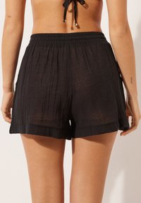 Black shorts made of lightweight, textured fabric with an elastic waistband, featuring a relaxed fit and subtle hem detailing.