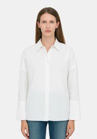 Camicia bianca con colletto classico e maniche lunghe. Realizzata in tessuto morbido, presenta una vestibilità rilassata e dettagli di cucitura discreti.