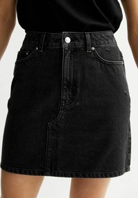Zwarte denimrok met een hoge taille, voorzakken, sluiting met zilveren knoop en contrasterende stiksels, met een licht gestructureerde afwerking.