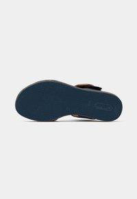 Brown leather sandal with navy rubber sole. Velcro strap adjustable for fit. Textured bottom for traction. Minimalist design, open toe.