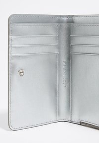 Silver leather wallet interior featuring multiple card slots, a snap closure, and embossed branding on smooth textured material.