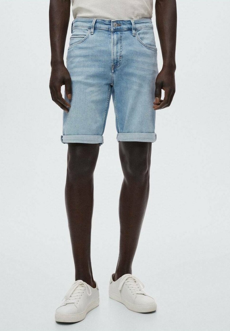 Shorts en denim bleu clair avec ourlets retroussés, cinq poches et détails de couture subtils. Portés avec des baskets blanches et un haut clair.