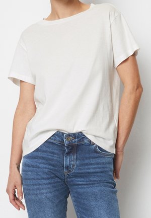 Lys beige kortærmet t-shirt i blødt bomuldsstof med løs pasform og rund halsudskæring, kombineret med blå denimjeans.