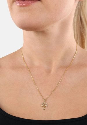Collier en or avec un pendentif en forme d'arbre orné de petites pierres précieuses, porté par une femme portant un haut noir.