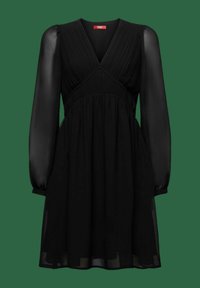 Robe noire à manches longues avec manches bouffantes transparentes, col en V, corsage froncé et jupe fluide sur fond vert uni.