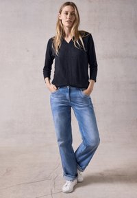 Schwarzes Langarmshirt mit V-Ausschnitt, kombiniert mit hellblauen, lockeren Jeans und weißen Sneakers. Glattes Material und lässige Passform.