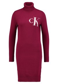 Fuchsia stickad klänning med hög polokrage, långa ärmar, ribbade mudd och en vit "CK"-logga på bröstet. Stickad textur.