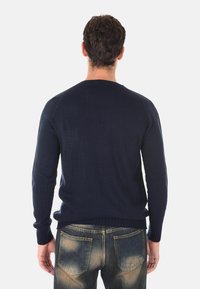 Maglione lavorato a maglia blu navy con maniche lunghe e polsini a costine, abbinato a jeans in denim chiaro sbiaditi, visto da dietro.