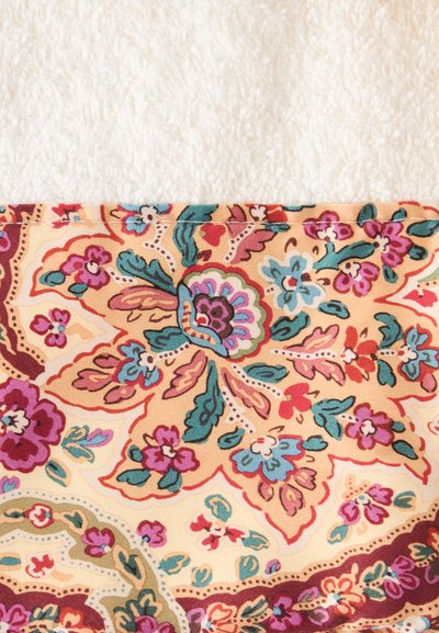 Tissu blanc doux texturé à côté d'un tissu à motif floral coloré avec des fleurs roses, bleues, vertes et rouges sur fond beige.