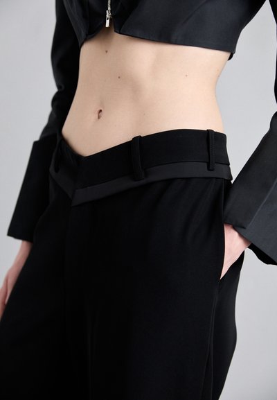 Black tailored pants with a flat waistband featuring two loops, made of smooth fabric; paired with a cropped black jacket.