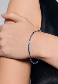 Srebrna bransoletka ozdobiona na przemian niebieskimi i przezroczystymi kryształami, charakteryzująca się smukłym, elastycznym kształtem, który dopasowuje się do nadgarstka.