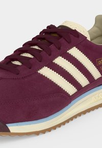 Sneaker en daim bordeaux avec bandes crème Adidas, lacets bordeaux, semelle bleue et crème, et languette texturée.