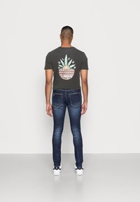 Camiseta gris oscuro con un diseño gráfico colorido y jeans azules de corte slim con un desvanecimiento mínimo, combinados con zapatillas blancas.