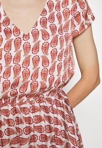 Bloemmotief jurk met een V-halslijn en korte mouwen, gemaakt van lichte stof in roze met rode en gouden paisley-ontwerpen.