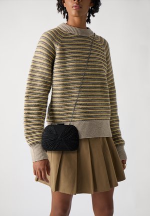 Randig stickad tröja i beige och oliv, matchad med en plisserad olivkjol. En liten svart clutch med texturerad detalj bärs över kroppen.