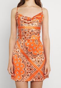 Oranges Satin-Minikleid mit Spaghettiträgern, das mit Paisley- und Blumenmustern in Schwarz und Weiß verziert ist. Glatte Textur, taillierter Schnitt.