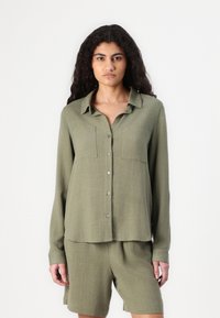 Olijfgroene, lang-sleeve shirt met twee borstzakken en knopen, gemaakt van een gestructureerde stof. Gepaarde met bijpassende shorts.