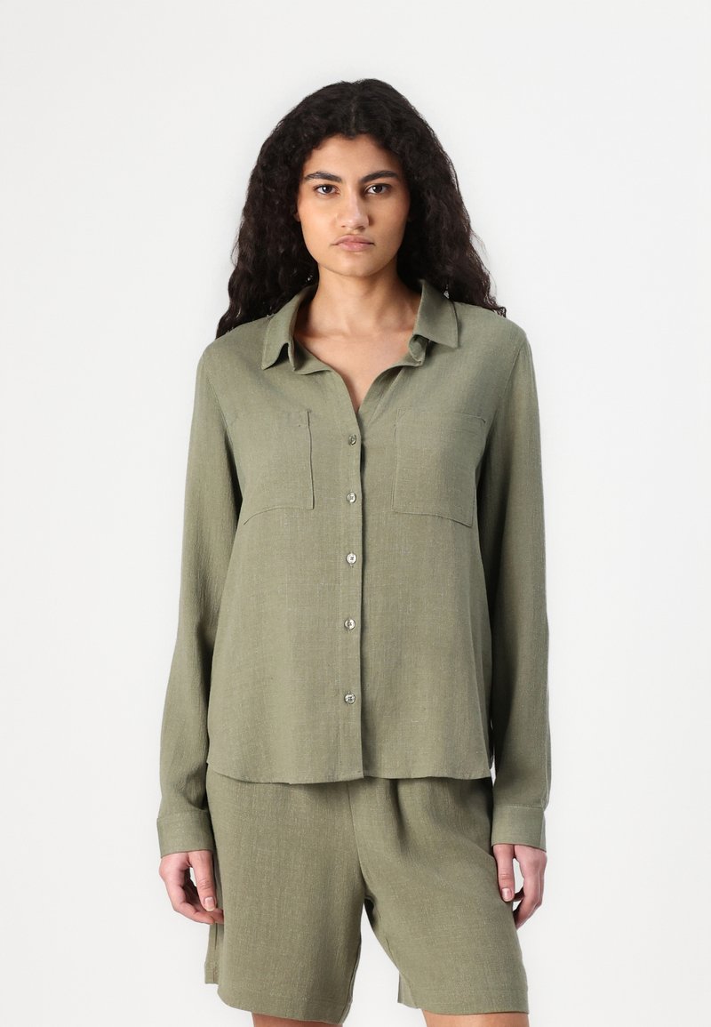 Olijfgroene, lang-sleeve shirt met twee borstzakken en knopen, gemaakt van een gestructureerde stof. Gepaarde met bijpassende shorts.