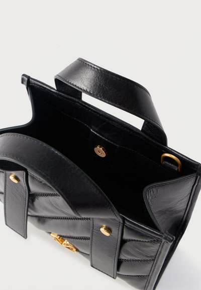 Μαύρη δερμάτινη γυναικεία τσάντα με χειρολαβές στο πάνω μέρος, χρυσά μεταλλικά στοιχεία και ανοιχτό εσωτερικό που δείχνει κλείσιμο με μαγνητικό κούμπωμα.