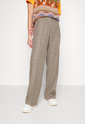 Personne portant un pantalon large à carreaux beige, des baskets blanches, un gilet à motif orange et une chemise jaune à manches courtes.