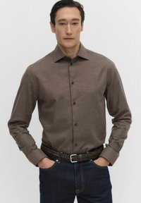 Brun långärmad skjorta med knäppning och texturerad tyg. Kombination med mörka denimjeans och ett flätat bälte.