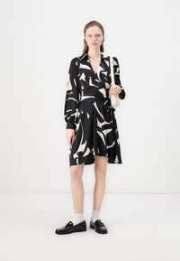 Black dress with abstract white patterns, long sleeves, collar, and a tied waist. Paired with black shoes and light socks.