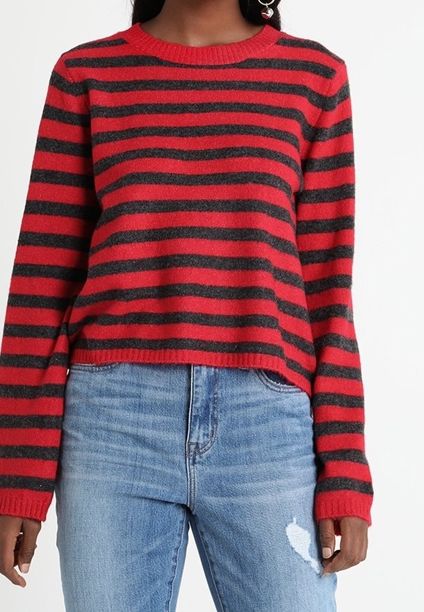 Femme portant un pull à rayures horizontales rouges et noires à manches longues et un jean bleu clair déchiré.