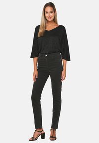 Čierny, trblietavý, voľnejší top s výstrihom do V a 3/4 rukávmi, kombinovaný s čiernymi džínsami s vysokým pásom a sandálmi na vysokom podpätku.