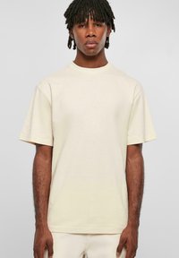 Tricou cu mânecă scurtă din bumbac bej deschis, având un gât rotund și o croială lejeră, cu o textură netedă și fără modele vizibile.