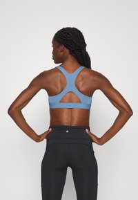 Sutiã desportivo azul com um design de costas nadadora e detalhe recortado. Usado com leggings pretos de cintura alta, destacando uma textura suave.