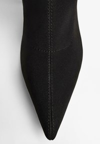 Czarny but na spiczu wykonany z gładkiego materiału, z widocznym przeszyciem wzdłuż cholewy oraz smukłą sylwetką. Brak dodatkowych elementów ozdobnych.