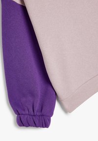 Due sezioni di tessuto: una rosa chiaro e una viola intenso. La sezione viola presenta un polsino arricciato, entrambi sono morbidi al tatto e lisci.