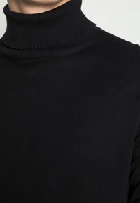 Schwarzer Rollkragenpullover, gerippte Textur, taillierte Passform, hoher Kragen und nahtlose Details, aus einem weichen, dehnbaren Stoff gefertigt.